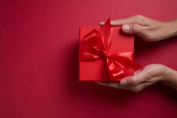 istock Hand holding the red gift box with a red bow on a red background, element for design with copy space for text or image 2194179975