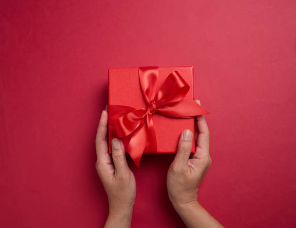 istock Hand holding the red gift box with a red bow on a red background, element for design with copy space for text or image 2194180074