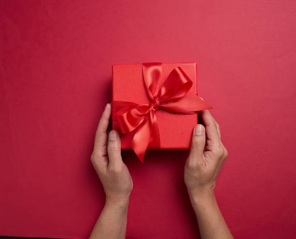 istock Hand holding the red gift box with a red bow on a red background, element for design with copy space for text or image 2194180129