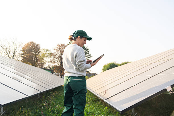 istock Female farmer stands next to solar panels. Modern agricultural farm using solar panels. Agricultural silos in the background. 2194181131