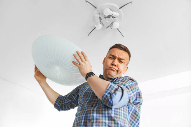 istock A man in a plaid shirt holds a large white round ceiling lamp in his hands. 2194183966