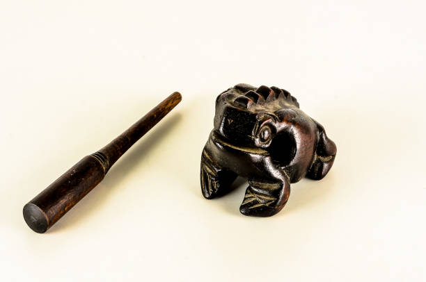 A frog figurine sits on a white surface next to a wooden stick