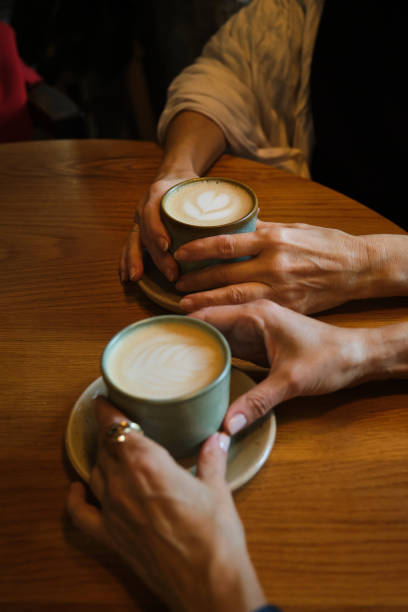 istock Two women holding cappuccino cups at a cafe table 2194191671