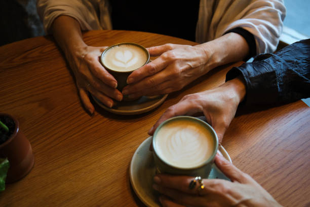 Three women are holding their cappuccinos on a wooden table at a cafe