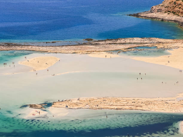 This landscape photo was taken, in Europe, in Greece, in Crete, in Balos, At the edge of the Mediterranean Sea, in summer. We see the fine sandy beach with pink reflections at the foot of the rocky cliffs, under the sun.