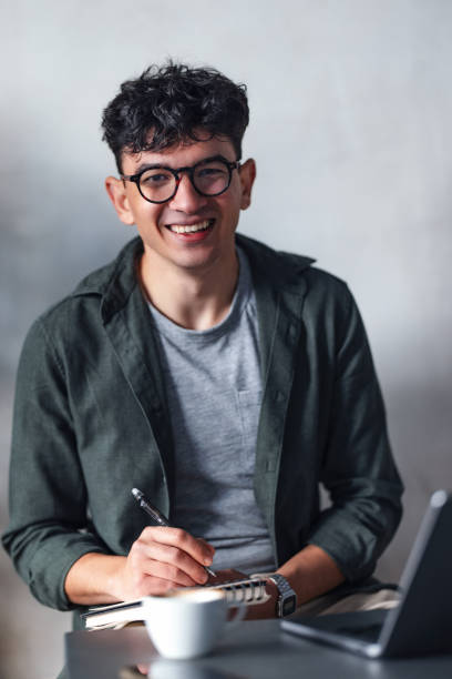 istock Smiling Man Writing Notes in a Cafe Setting with Laptop and Coffee 2194195552