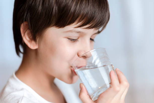 istock Cute boy drinking water from glass at home on white background 2194195827