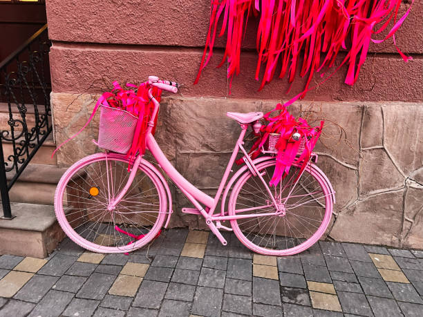 A vibrant pink bicycle decorated with colorful ribbons stands out against a stone wall, creating a cheerful and artistic scene. This decorative setup captures joy, creativity, and urban charm.