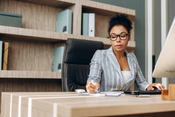 istock Serious businesswoman working on computer and taking notes in modern office 2194199166