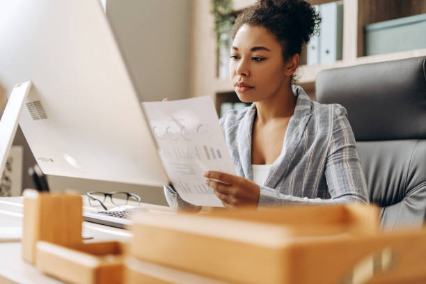 Focused businesswoman analyzing charts and graphs on paper in modern office