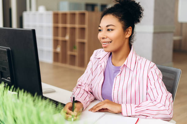 istock Smiling African American woman it specialist taking notes while working on computer in modern office 2194199778