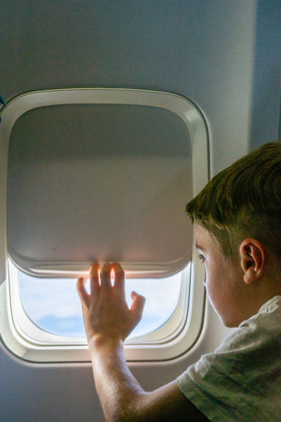 Young passenger opening airplane window blind during flight