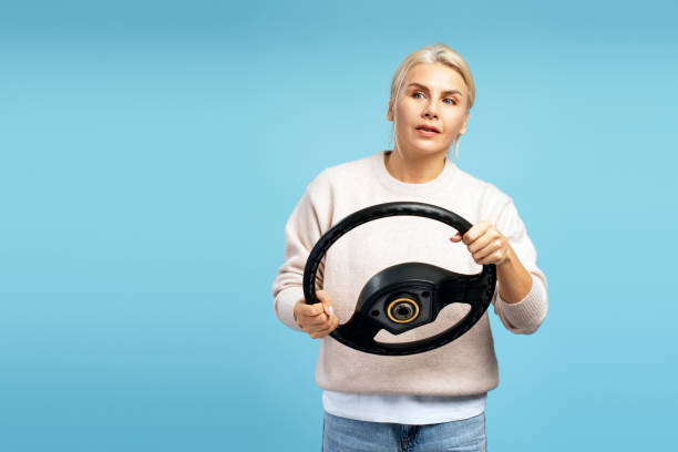 istock Woman holding steering wheel, simulating driving a car on blue background 2194201417