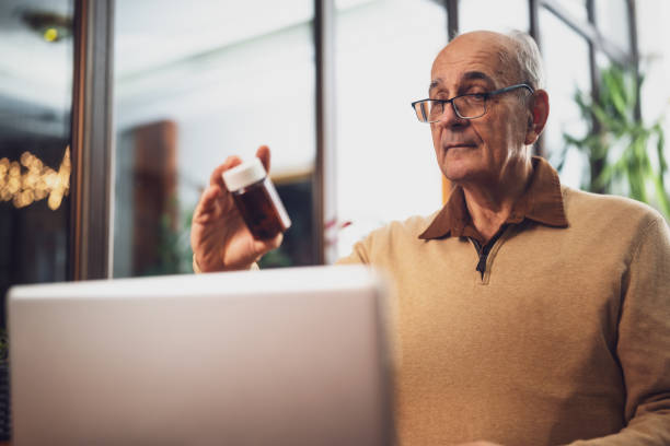 istock Older man with eyeglasses holding bottle of pill and using laptop 2194202189