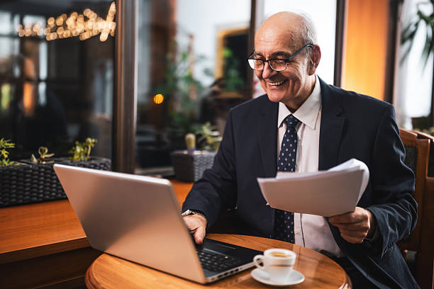 istock Confident senior entrepreneur using laptop and reviewing documents in cafe 2194202727