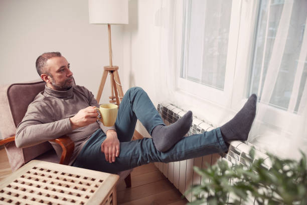 istock Man with tea cup holding feet with socks on a home heating radiator on a cold winter day outdoors. 2194204252