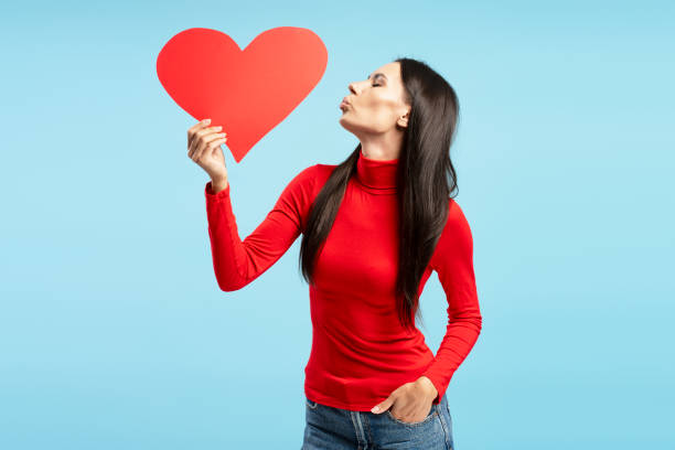 istock Beautiful woman kissing a red heart on blue background 2194209607