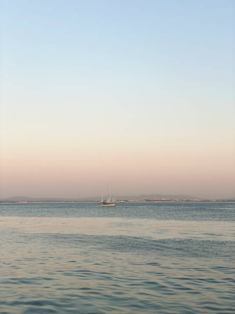 Serene seascape with a sailboat on calm waters during sunset. Soft pastel sky blends into the horizon, evoking tranquility and minimalism.