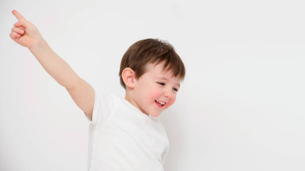 istock Smiling child pointing upwards with raised arm on white background. Studio portrait photography with copy space. Childhood happiness and playful moment concept. Design poster, banner, greeting card, 2194217680