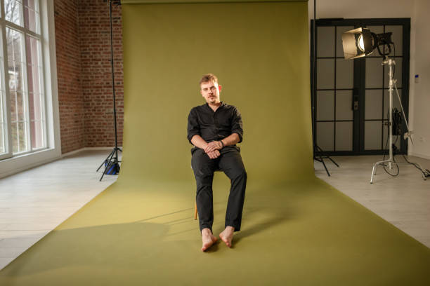 istock Barefoot man sitting casually in spacious photo studio. 2194219926