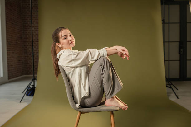 This modern portrait in a studio setting showcases a woman in a relaxed pose on a chair against a green backdrop, embodying tranquility and artistic simplicity.