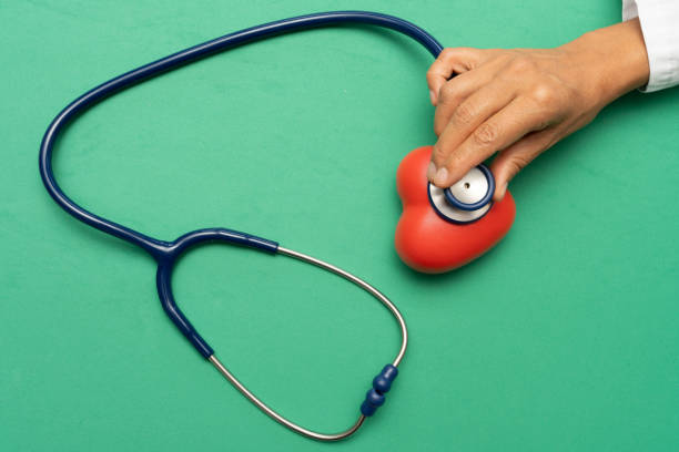 Medical professional listening to red heart using stethoscope against green surface