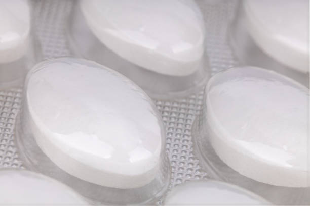 Some vitamins in blister packs on a rich shiny rosewood table. There are both Vitamin D3 in Blue and B Complex in Red. Shot in a studio environment with natural light. Long Exposure. Copy space. Note to Inspector: All logos, brand names and batch numbers have been removed.