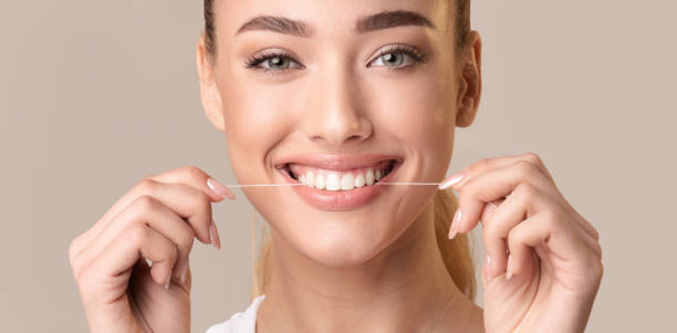 istock Smiling Woman Demonstrating Dental Flosser Usage in a Light Background 2194235568