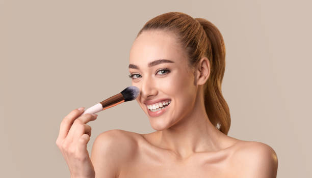 istock Smiling Woman Applying Makeup With Brush Against Neutral Background in Beauty Routine 2194235580
