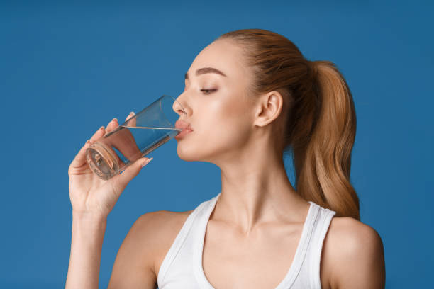 istock Woman Enjoying a Refreshing Drink of Water Against a Solid Blue Background 2194235622