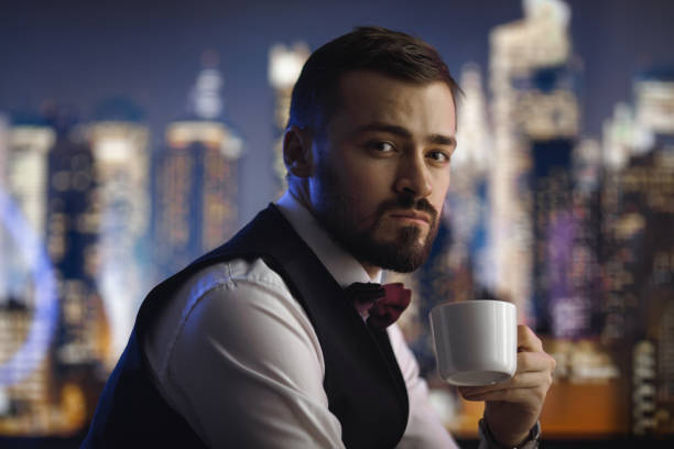 Portrait of a confident man in formal attire holding a cup of coffee, with a blurred city skyline glowing at night. Perfect for lifestyle, business, or urban-themed promotional visuals.