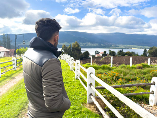Rear view of an adult man, with a relaxed attitude, contemplating the landscape from a hill on a bright spring day, surrounded by green fields and a gentle breeze.