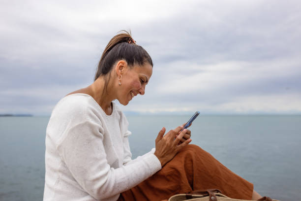 istock Happy woman using a smartphone by the sea on a cloudy day 2194244813