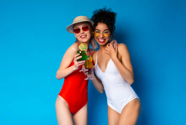 istock Two Friends Enjoy Tropical Drinks in Stylish Swimsuits Against a Bright Blue Backdrop 2194246072