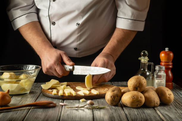 istock Chef cuts raw potatoes into pieces with a knife before preparing breakfast or dinner. Close-up of a cook hands while working in a restaurant kitchen 2194250522