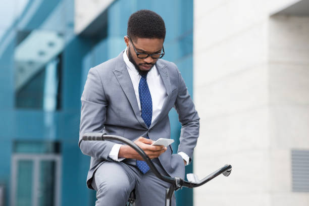 istock Man in Business Suit Checking Phone While Sitting on Bicycle in Urban Setting 2194252679