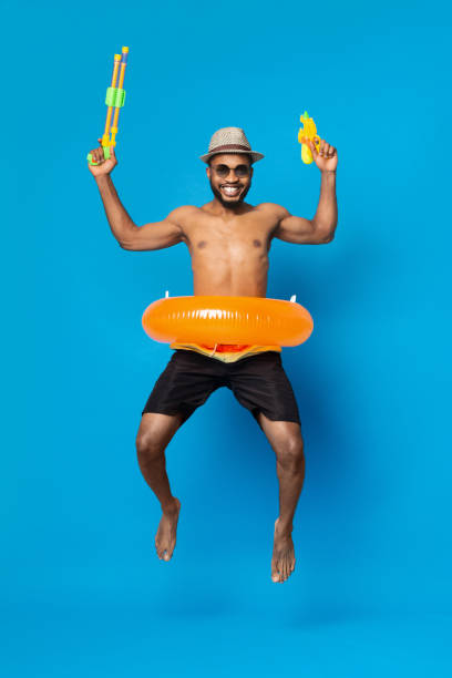 istock Cheerful young black man jumping with two water guns 2194253131