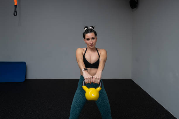 Female athlete executing powerful kettlebell swing, displaying muscular strength during high-intensity gym training. Concentrated movement expressing athletic prowess and physical conditioning
