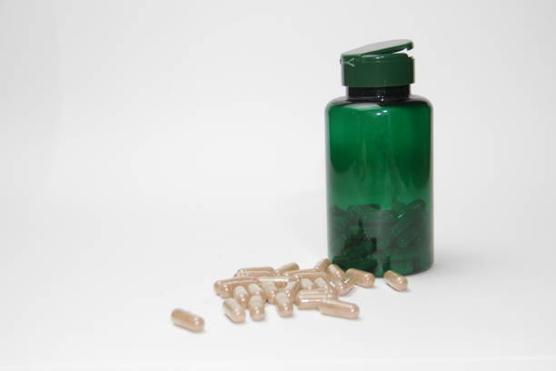 A green plastic supplement bottle with beige capsules spilling out onto a white background, symbolizing health and wellness. Ideal for concepts related to nutrition, dietary supplements, and holistic well-being.