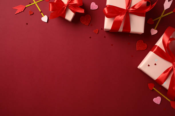 istock Valentine's Day concept with three gift boxes wrapped in red ribbons, surrounded by heart-shaped decorations and Cupid's arrows on a red background 2194264337