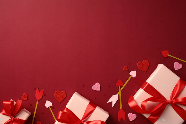 istock Valentine's Day flat lay composition with red and pink hearts, arrows, and pink gift boxes wrapped in red ribbon on a red background 2194264372