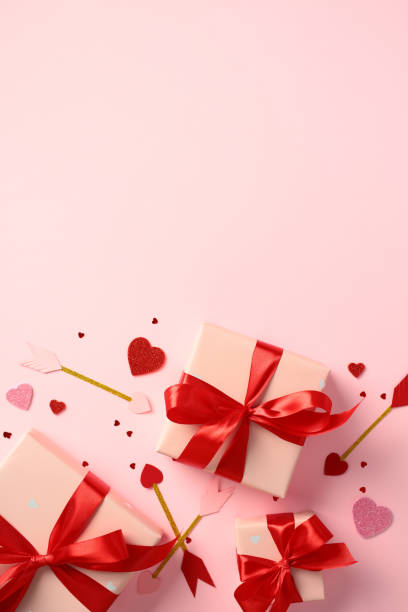 istock Valentine's Day flat lay composition with three pink gift boxes tied with red ribbons, surrounded by glitter hearts and arrows on a pink background 2194264386
