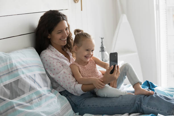 istock Cheerful mother rest on bed with daughter use smartphone 2194265193