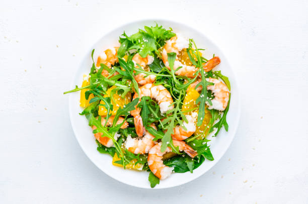 istock Shrimp salad with orange, arugula and sesame seeds on white background. Top view 2194269740
