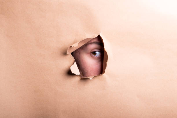 istock Man eye looking through a hole in a sheet of paper. 2194272494