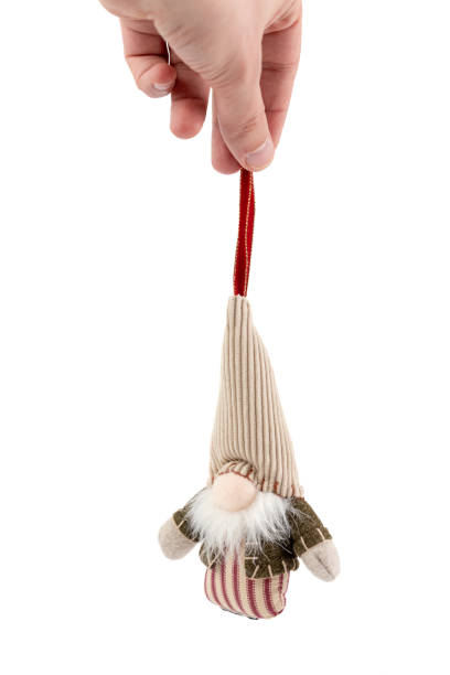 close-up on a white background a man's hand holds a textile soft Christmas tree toy in the form of a forest gnome with a large cap pastel colors modern decor