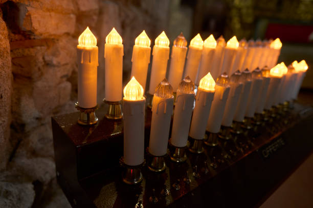 Rows of electric candles glowing warmly in a dimly lit stone church interior, creating a serene and spiritual atmosphere.