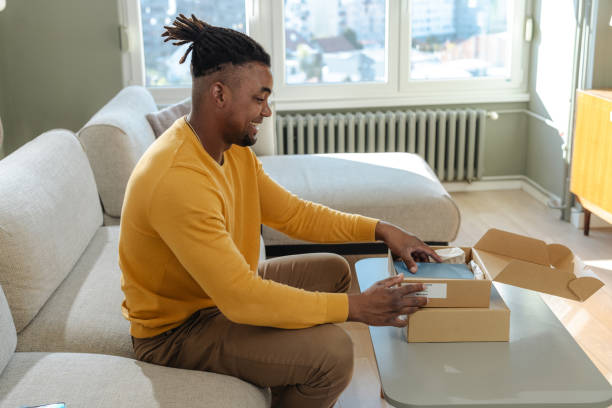 istock Man delightedly unpacking a package on the sofa in a bright living room 2194279608