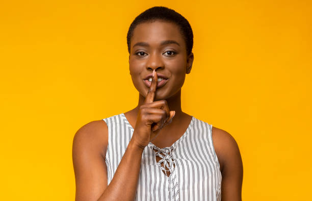 istock Woman Making a Shushing Gesture Against a Vibrant Yellow Background in a Studio Setting 2194291535