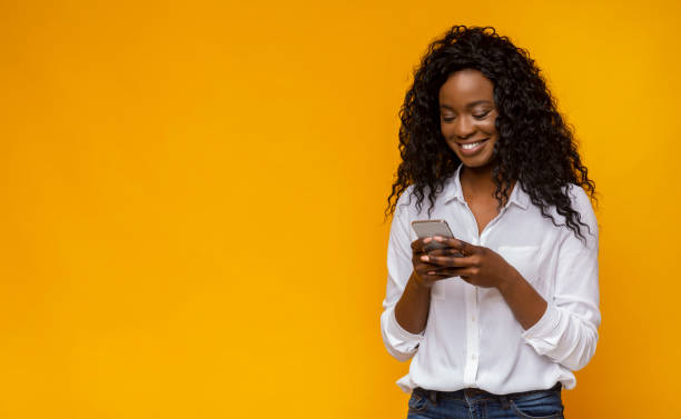 istock Smiling Woman Using Smartphone Against a Bright Yellow Background in Urban Setting 2194291612